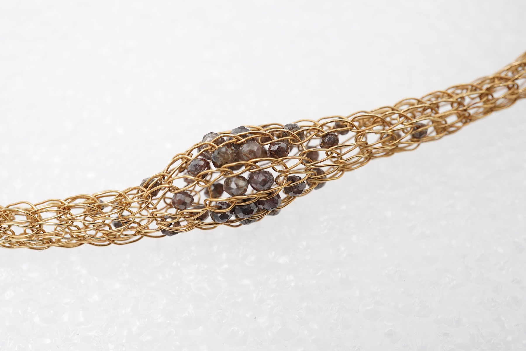 An 18ct gold and diamond necklace, composed of a woven tube of 18ct gold wire links, three sections threaded with brown diamond beads, length approximately 45cm, British hallmarks, sponsor's mark TJH, gross weight approx